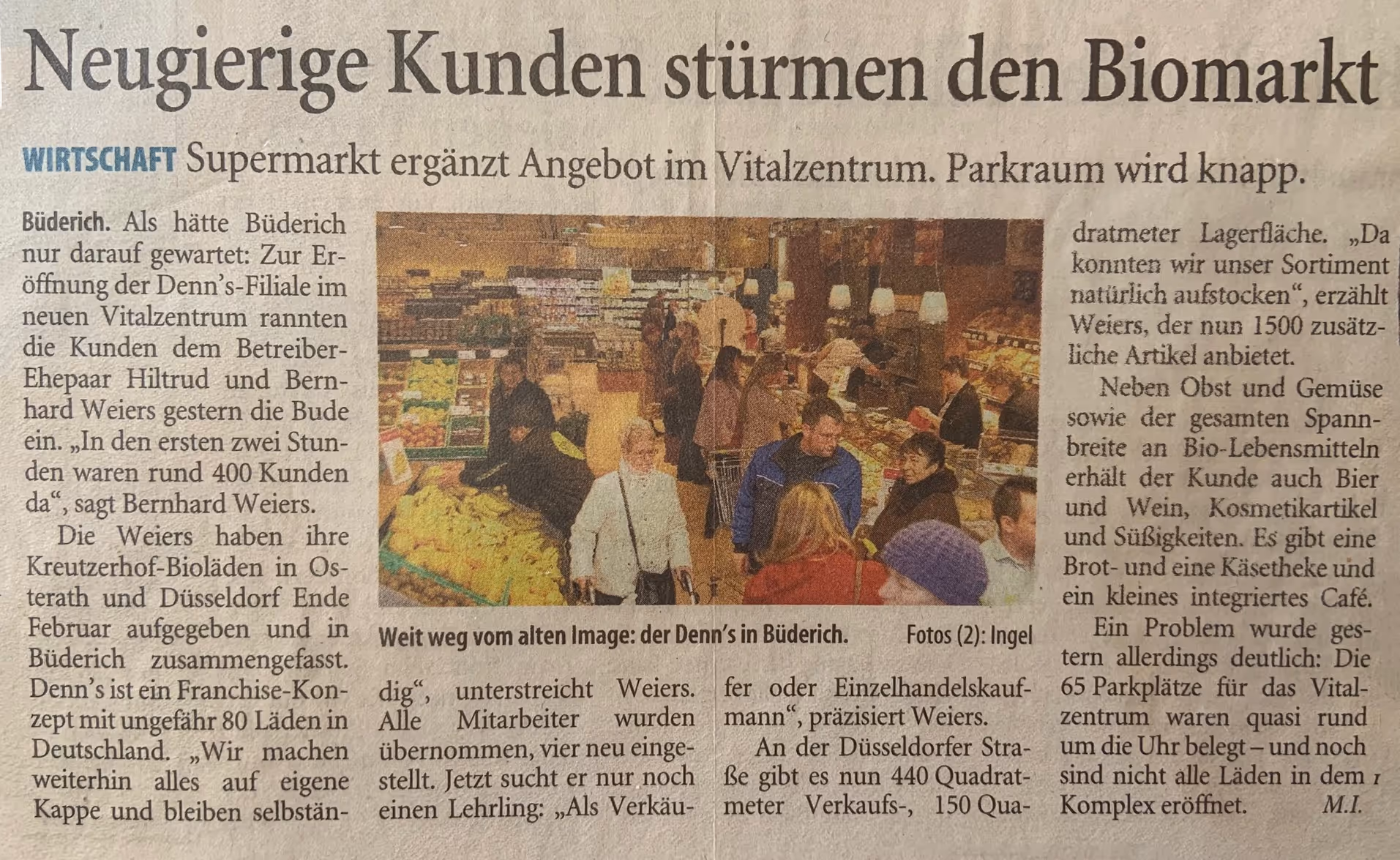 Voller Biomarkt mit mehreren Kunden, die an Obst- und Gemüseständen sowie anderen Regalen einkaufen.